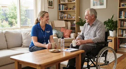 Support worker in blue polo having coffee conversation with participant in wheelchair